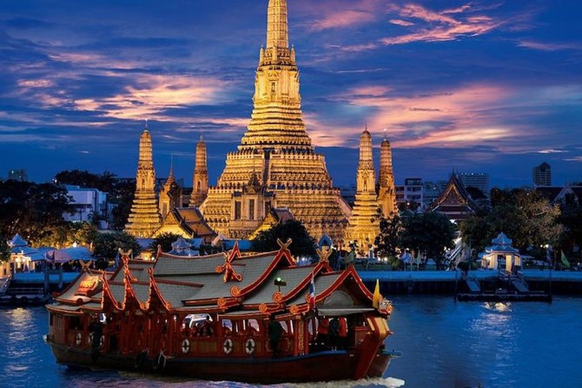 Barco de cena navegando de noche frente al templo Wat Arun iluminado, Bangkok