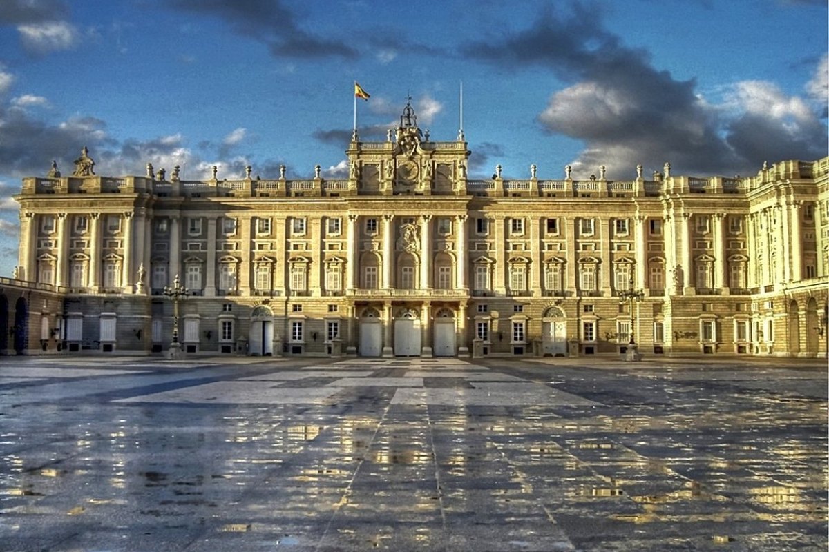 Fachada del Palacio Real de Madrid con la plaza mojada reflejando el cielo