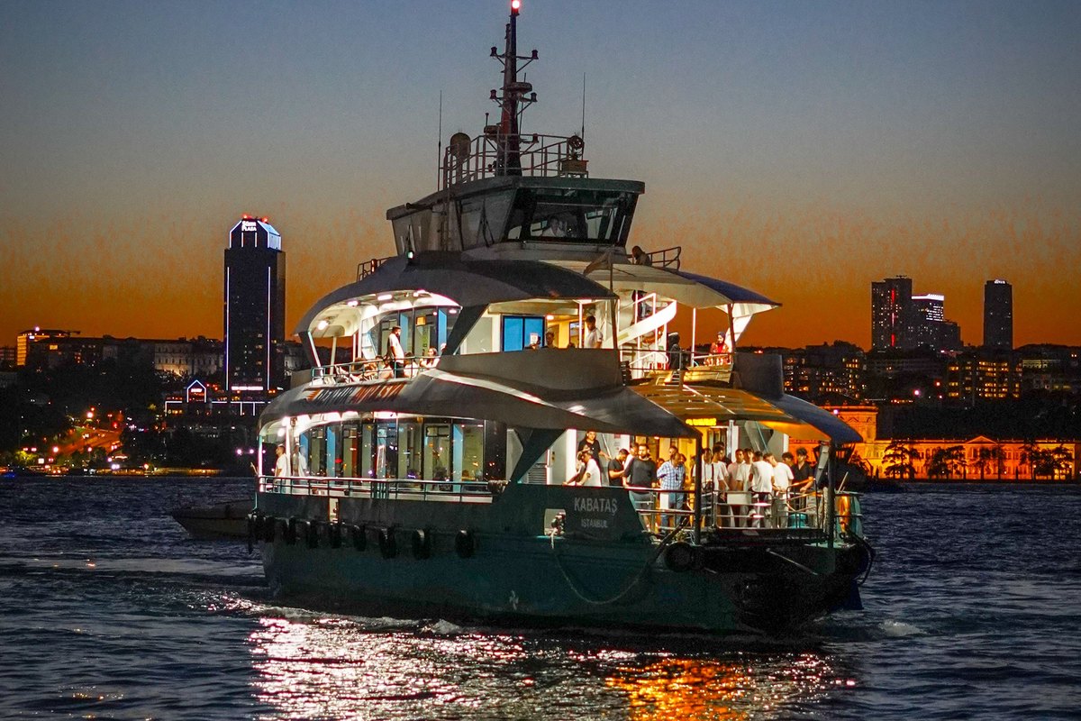 Yate iluminado navegando de noche con el skyline de fondo